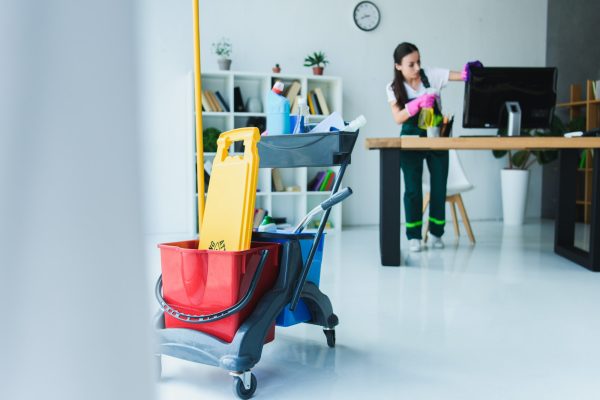 young-female-janitor-cleaning-office-with-various-cleaning-equipment.jpg